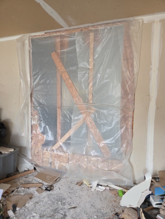 Plastic sheeting covers the large opening in the wall that separates the garage from the home interior