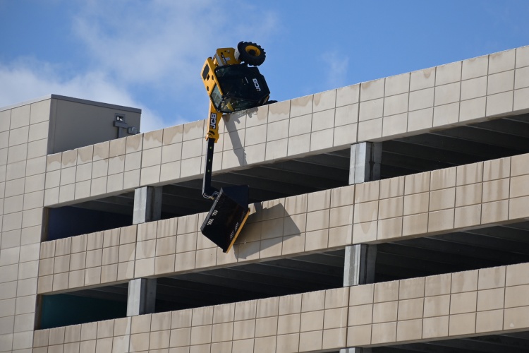 A telehandler dangles over the top edge of a 7-story parking ramp