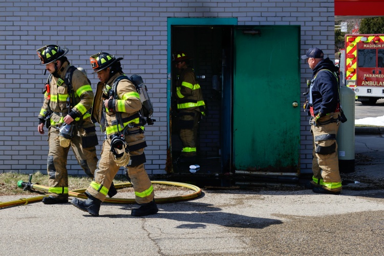 Two firefighters walk by the car wash building as a third looks inside