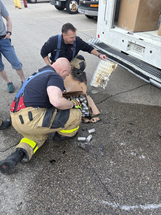 a fire investigator holds a burned piece of packaging while another investigator examines the battery cells