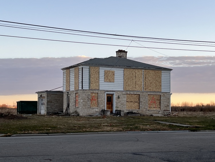 Two-story farm house with windows boarded up