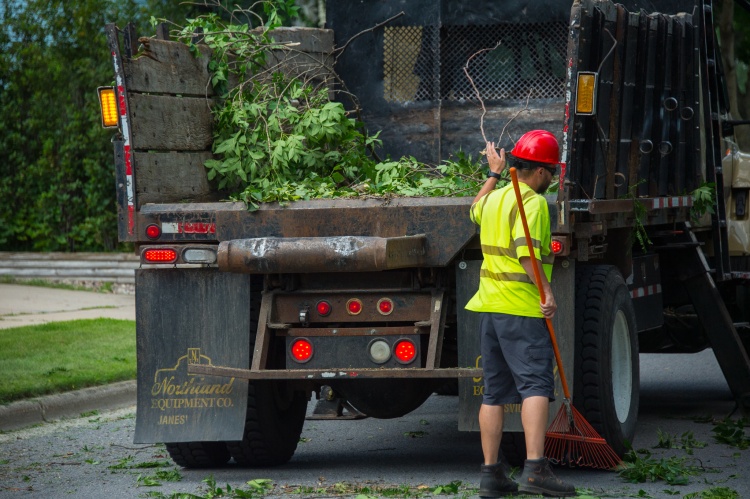 A City employee loads storm debris into the back of a large truck