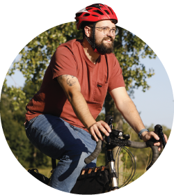 Man riding a bicycle outdoors while wearing a red helmet and a T-shirt.