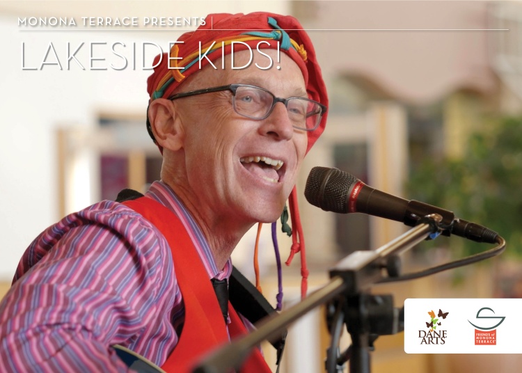 Man in colorful striped shirt, suspenders & beanie smiling & singing into a microphone i