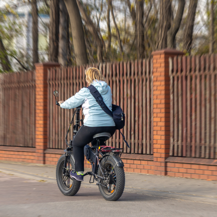 Woman riding a fat-tire e-bike on a paved path outdoors.