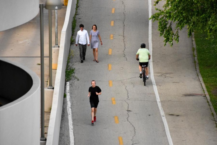 Image of a multi-use path showing several walkers and a jogger on the left side of the split path coming towards the viewer, and one bicyclist on the right riding away from the viewer.