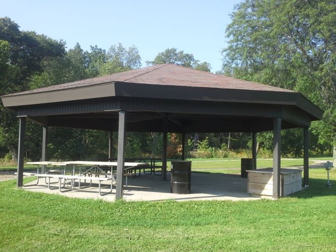 Small sun shelter with several picnic tables and trash bins.
