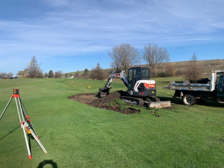 backhoe digging bunker with blue sky and green grass