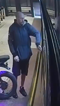 Man wearing shorts and a sweatshirt stands at a bus station before hitting and damaging a bus.