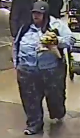 Woman wearing a long-sleeved shirt and pants and carrying an item, believed to be a suspect in a theft case.
