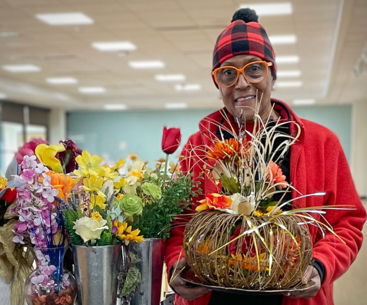 A woman holding a centerpiece and standing next to vases of bouquets.