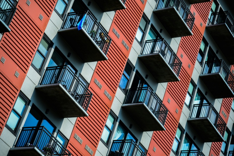 A section of a red and gray apartment building with small balconies.