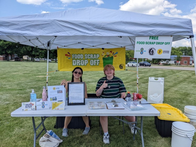 Two volunteers greet guests at the Farmers's Market Food Scrap Drop Off Site