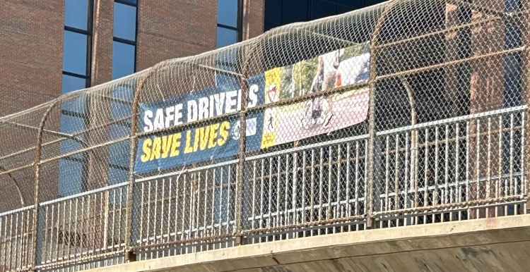 Banner hanging from pedestrian bridge over University Avenue that says "Safe Drivers Save Lives"