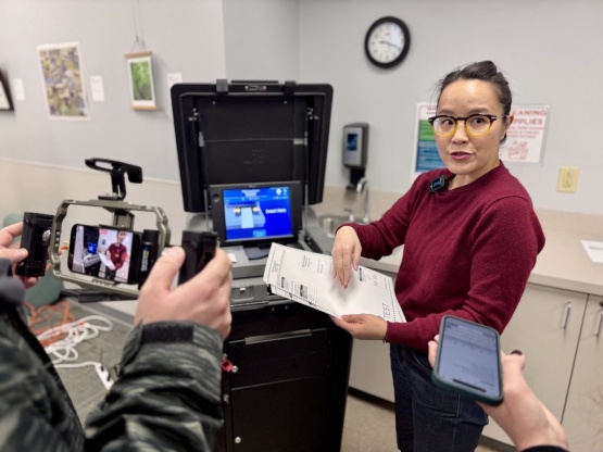 An election clerk standing in front of ballot tabulator with cameras in the foreground