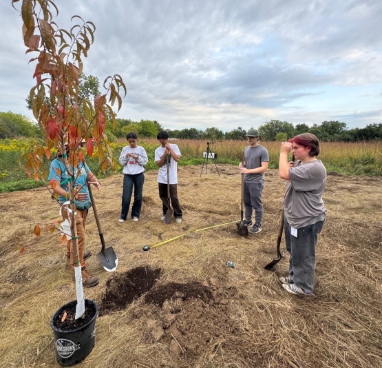  Youth prepare to plant the first tree of the food forest on a cloudy day
