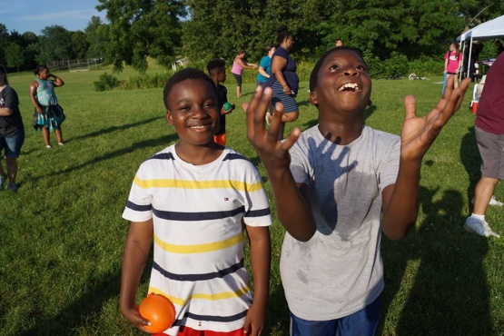 Two kids enjoying water balloons while other kids and adults are in the background