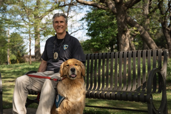Golden Retriever named Frost sits next to his police handler on a bench.