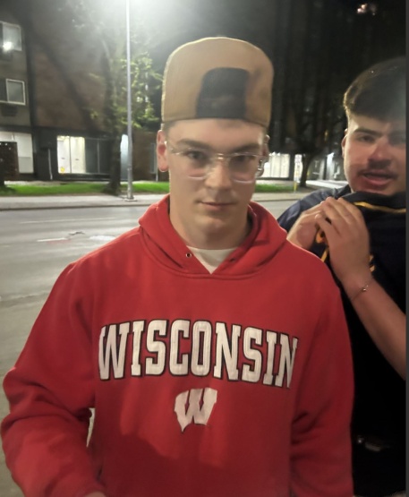 Suspects in a battery case, one wearing a red Wisconsin Badger sweatshirt and the other in a dark-colored shirt, stand before the vicitm.