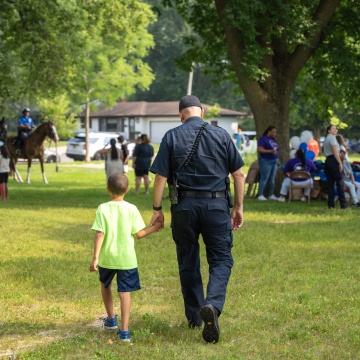 Madison police captain holds child's hand and walks at park during National Night Out celebration.