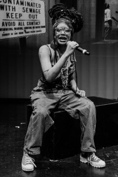 Octavia Ikard sits on a stage holding a mic while performing. They will serve as the WE READ Youth Voices Writing Contest Youth Ambassador for 2026.