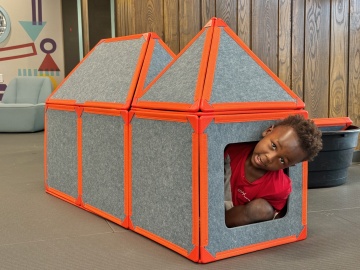 A child sticks their head out of a house-like structure they created using SuperSpace tiles at Pinney Library.