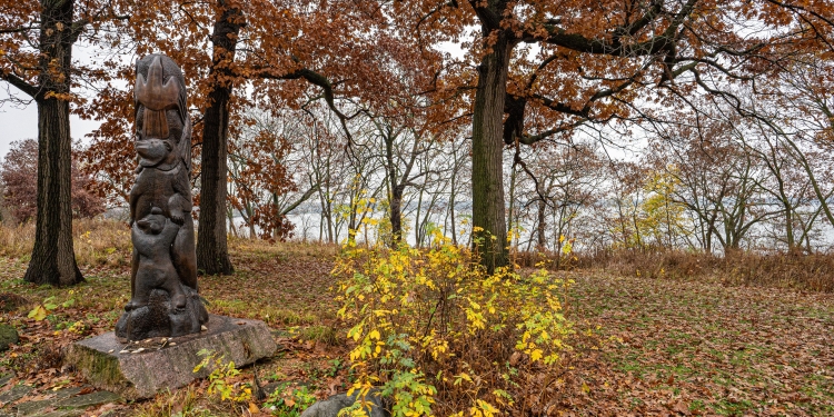 Orange and yellow fall leaves blanket the ground surrounding a wood carved memorial sculpture dedicated to the Ho-Chunk Nation.. 