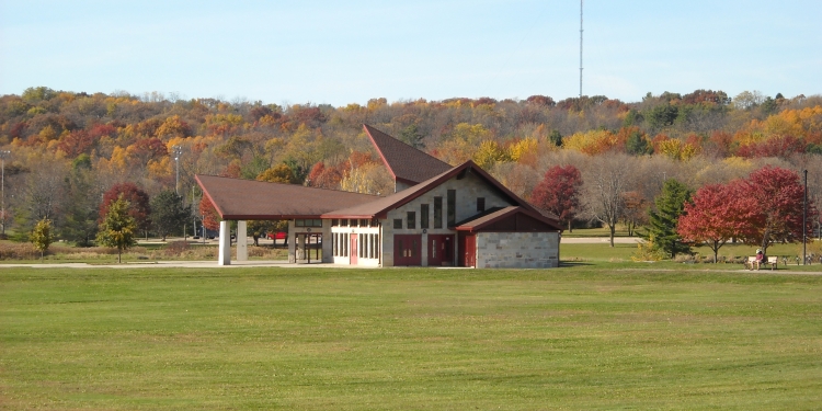 Shelter with green lawn, sidewalk, and road in front. Trees in background.