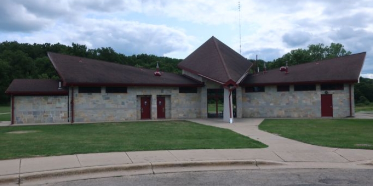 Shelter with green lawn, sidewalk, and road in front. Trees in background.