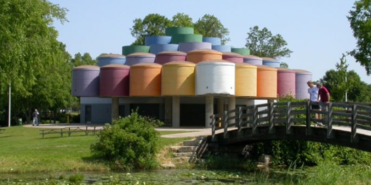 Shelter with multi-colored roof. Bridge over water with plants. 
