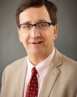 Finance Director David Schimiedicke, Caucasian male, brown hair, brown rimmed glasses, tan suit with red tie 