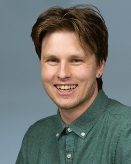 Alder Ochowicz is smiling and wearing a light green button up shirt. 