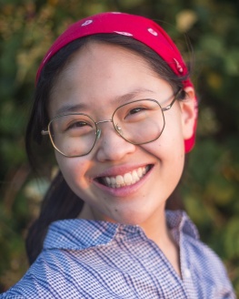 Alder Elect Ellen Zhang is smiling and wearing a red bandana around her head, a blue button up shirt and glasses