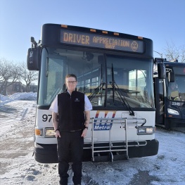 Metro Transit driver standing next to a bus in the winter with text that reads "Driver Appreciation Day" on the bus marquee.